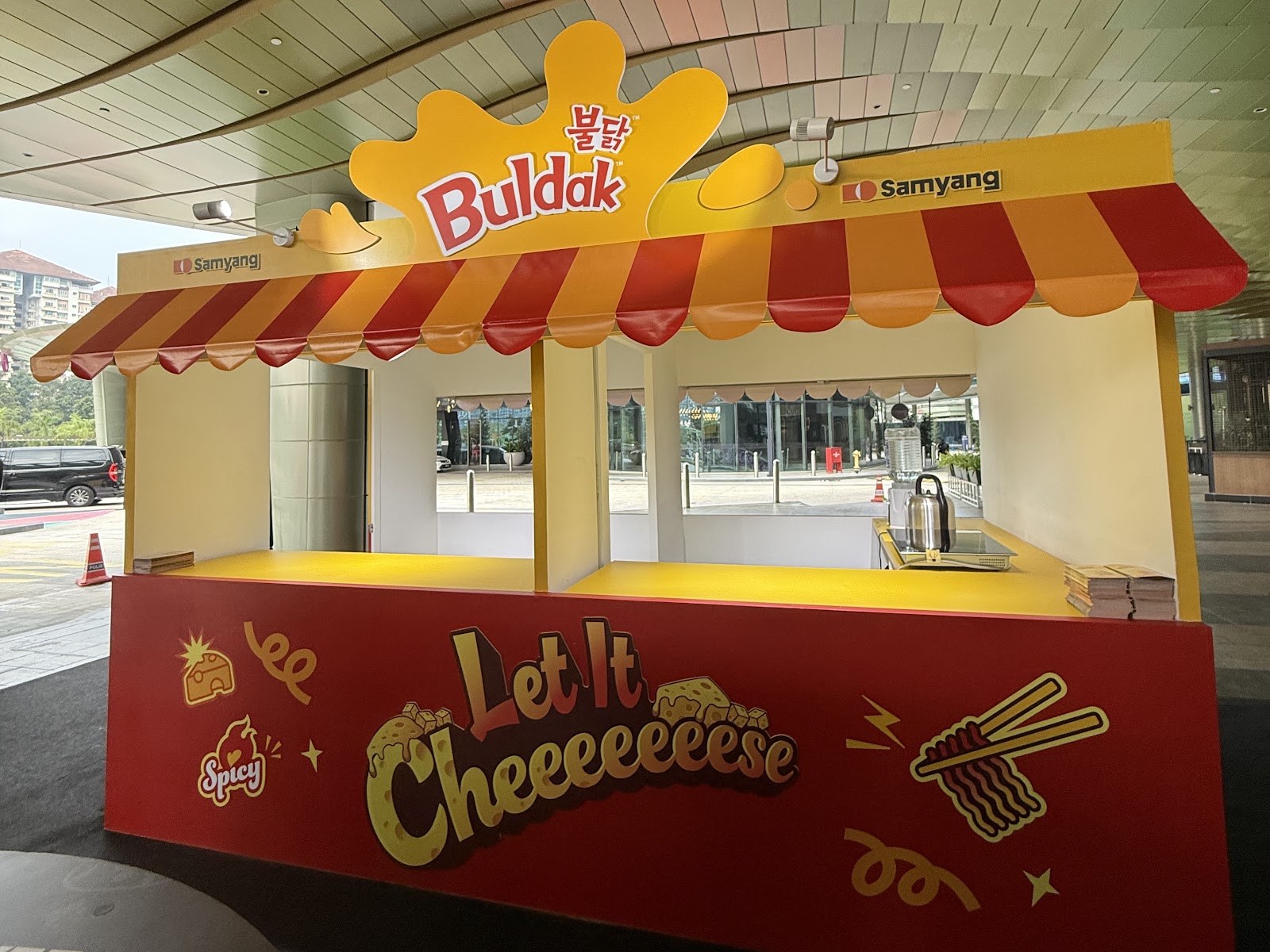 Samyang Buldak Let It Cheese refuel-station stall with a striped red-and-yellow canopy at a mall concourse roadshow